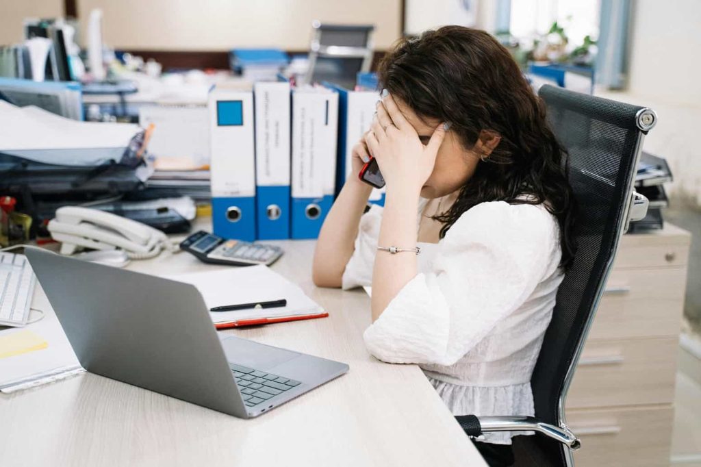 Freelance submergée à son bureau, illustrant la nécessité de faire le bilan de son activité professionnelle